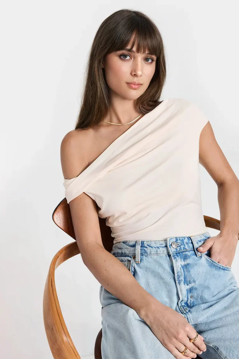Model wearing a cream off-shoulder top by Felipe Albernaz, paired with light-wash high-waisted jeans, showcasing contemporary casual fashion.